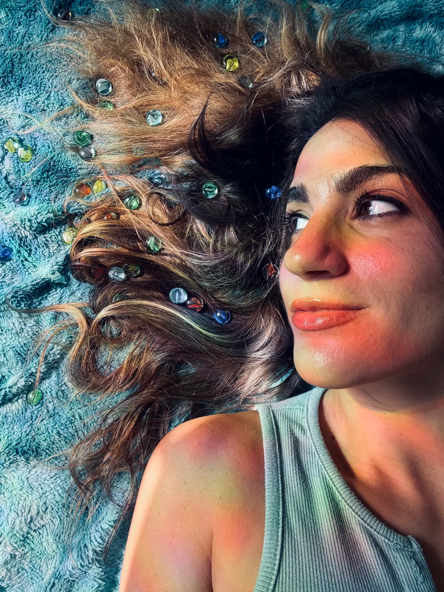 Lauren lying on a teal blanket, looking up, with coloured glass marbles scattered through her hair